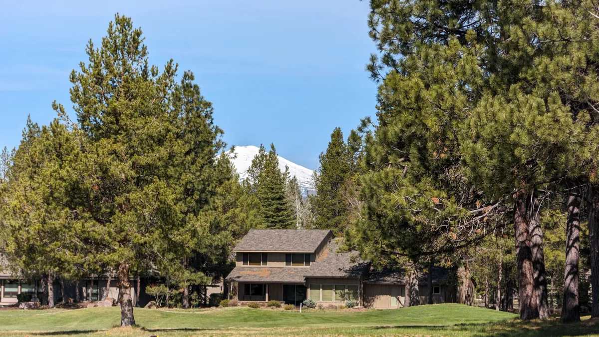 An inviting exterior view of the home, surrounded by tall trees with a mountain peeking behind. The yard is perfect for outdoor gatherings, while the deck area provides space for grilling and enjoying sunsets.
