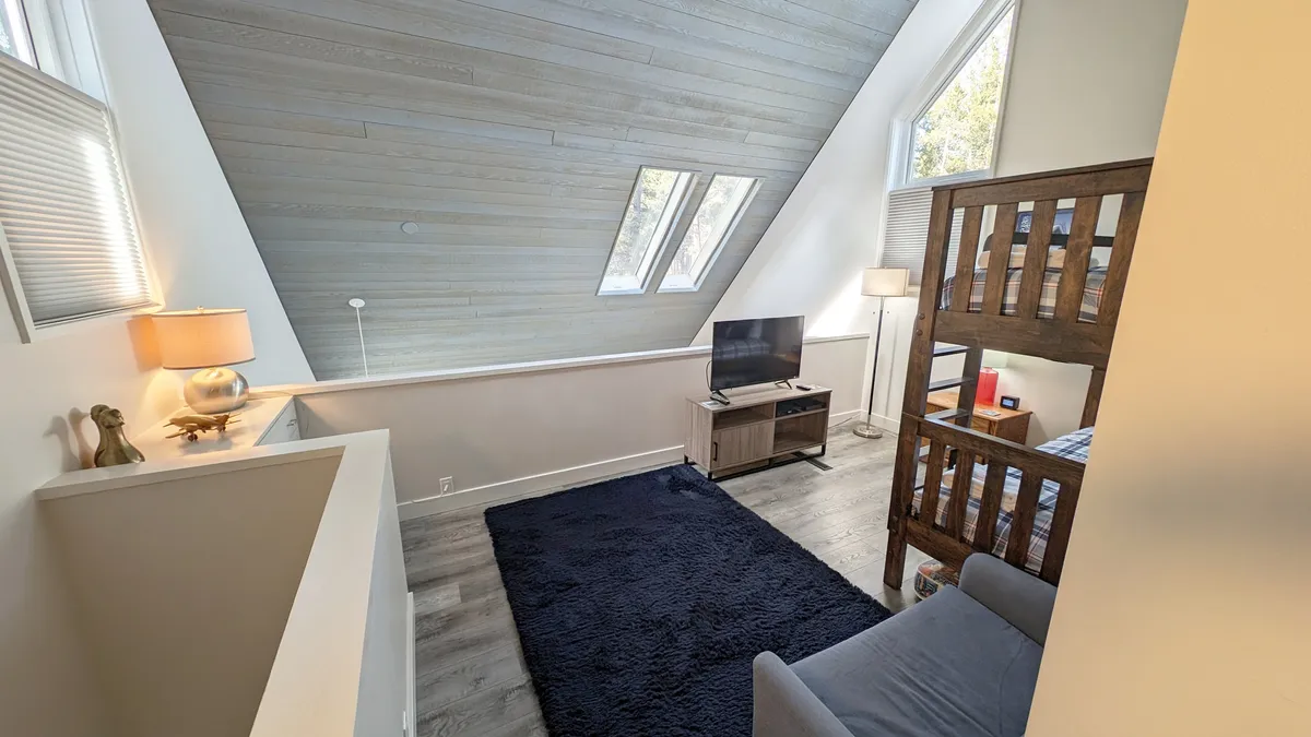 A cozy loft-style interior featuring a bunk bed, area rug, lamp, and television. The playful yet relaxed setting is ideal for family gatherings, movie nights, and a bonus sleeping or hangout space for kids after a day outdoors.