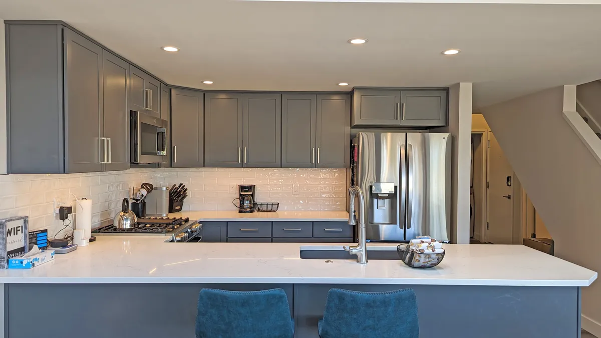 A sleek, remodeled kitchen with a central island, stainless steel appliances, grey cabinetry, and bar stools. The space is functional yet welcoming, ideal for cooking, entertaining, and socializing.