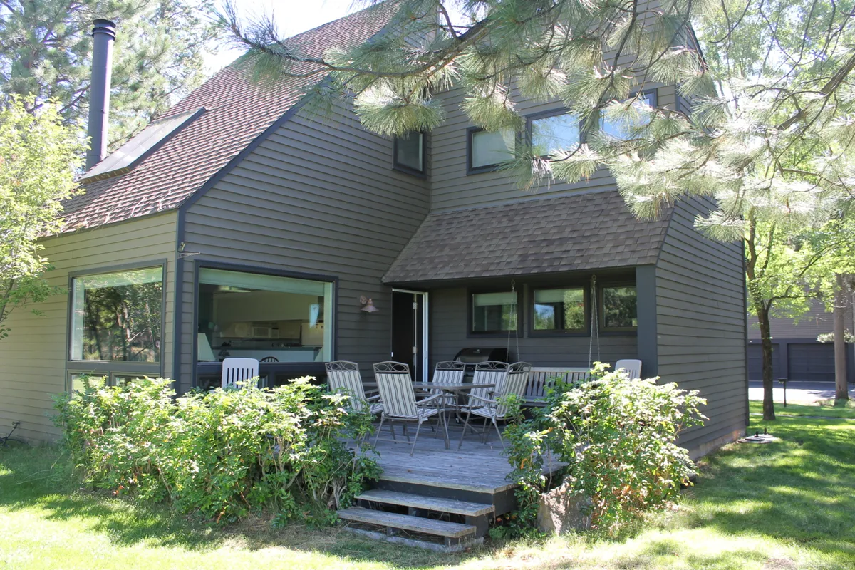 The photo captures a welcoming outdoor seating area on a deck, with large windows offering a glimpse into the house and lush greenery providing a serene backdrop. The arrangement encourages relaxation, social gatherings, and integration between indoor and outdoor living.