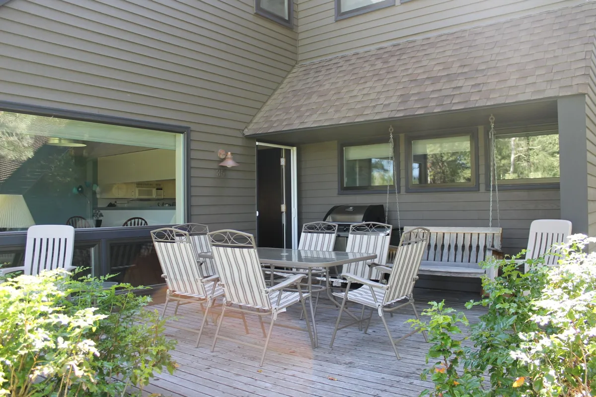 This image showcases a large deck with an outdoor dining table, a swing bench, a BBQ grill, and surrounding greenery. The setup invites gatherings and emphasizes the alfresco lifestyle, with plenty of space to relax, dine, and grill while enjoying the outdoors.