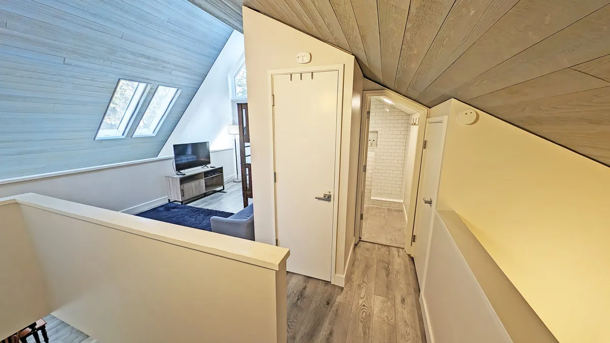 A cozy living area with a sloped wooden ceiling, large windows letting in natural light, a television unit, and comfortable seating—inviting guests to relax after a day of adventure. The Smart TV is clearly visible, emphasizing modern entertainment amenities.