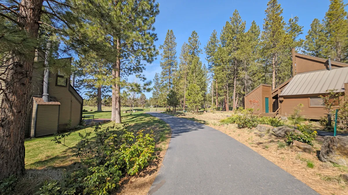 This image captures a peaceful pathway winding through tall trees, with houses nestled in the background. The open, tree-lined setting is perfect for biking, walking, or simply enjoying nature—activities highlighted in the section.